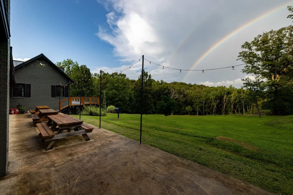 Picnic tables under string lights with a rainbow over the trees